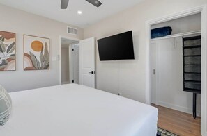 Ein Schlafzimmer mit einem Bett, einem Flachbildfernseher, einem Kleiderschrank und abstrakten Wandbildern.