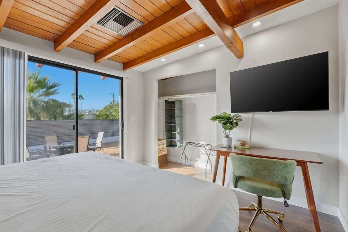 A bedroom with a large bed, a desk with a chair, a TV, and a sliding glass door leading to an outdoor area.