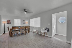 A dining area with a table and chairs, a ceiling fan, and a door with a circular window. - Sam Hughes Escape-Walk to U of A (Tucson)