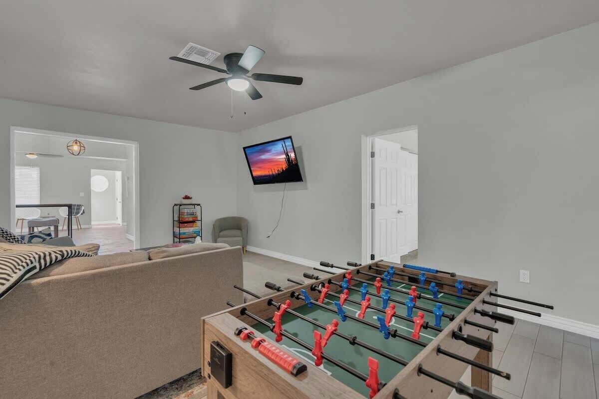 A room with a foosball table, a ceiling fan, a TV mounted on the wall, and a door leading to another room.