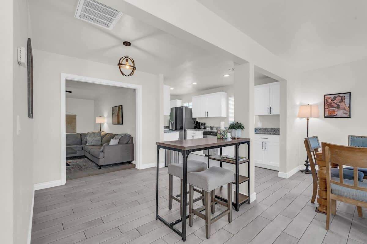 A modern kitchen with white cabinets, a dining table with two chairs, and a living area with a sofa and a lamp.
