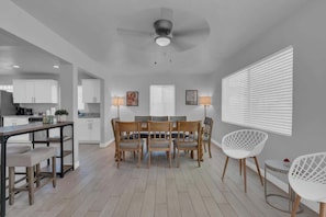 A modern kitchen with white cabinets, a dining area with a wooden table and chairs, and a ceiling fan. - Sam Hughes Escape-Walk to U of A (Tucson)