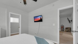 Ein Schlafzimmer mit einem Bett, einem an der Wand befestigten Fernseher und einer Tür zu einem weiteren Raum.