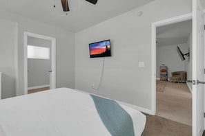 A bedroom with a bed, a television mounted on the wall, and a door leading to another room. - Sam Hughes Escape-Walk to U of A (Tucson)