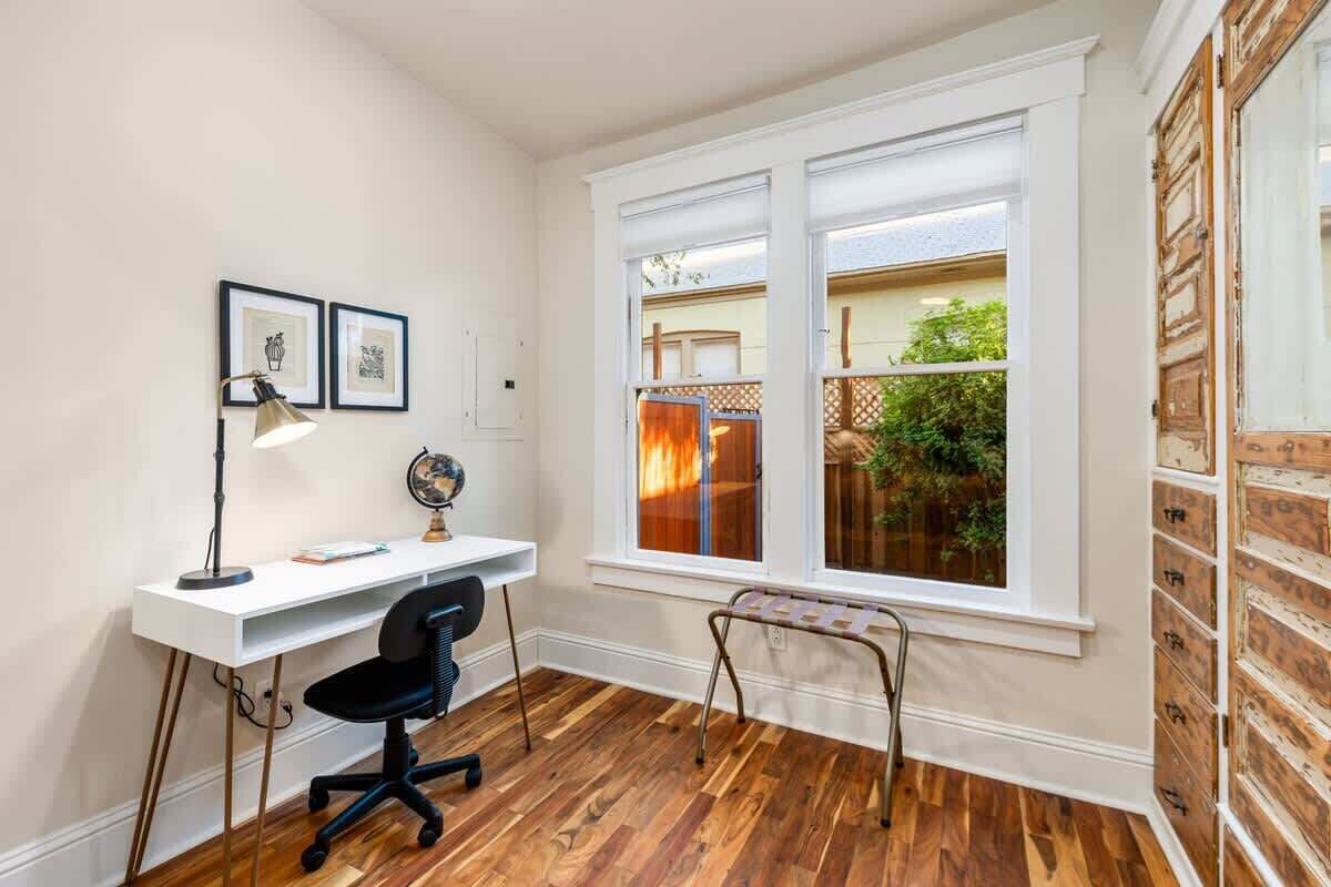 A room with a white desk, black office chair, and a window with a view of greenery.