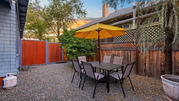 Eine Terrasse im Freien mit Tisch und Stühlen, einem gelben Sonnenschirm und einem Holzzaun.