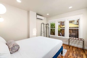 Ein Schlafzimmer mit einem Bett, einem Fenster mit Blick nach draußen, einer Klimaanlage und einem Metallradiator.