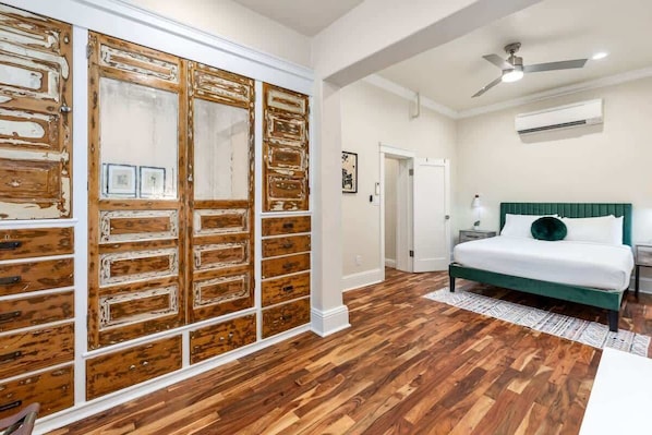 Une chambre avec une armoire en bois, un lit doté d’une tête de lit verte et un ventilateur de plafond.