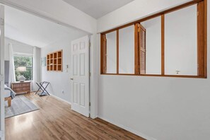 Ein Flur mit Holzboden, weißen Wänden und einem großen Fenster mit Jalousien.