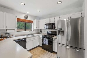 A modern kitchen with white cabinets, stainless steel appliances, a stove, and a refrigerator. - Bright & Spacious Family Retreat (Tucson)