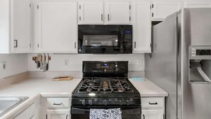 A kitchen with white cabinets, a black microwave, a stainless steel refrigerator, a gas stove, and a sink. - Bright & Spacious Family Retreat (Tucson)
