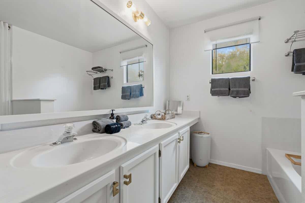 A bathroom with two sinks, a large mirror, and a window with towels.