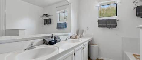 A bathroom with two sinks, a large mirror, and a window with towels.