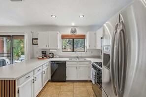A modern kitchen with white cabinets, a dishwasher, a stove, and a large refrigerator. - Bright & Spacious Family Retreat (Tucson)