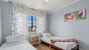 A bedroom with two beds, a window with curtains, a bedside table with a lamp, and a wall-mounted abstract painting. - Bright & Spacious Family Retreat (Tucson)