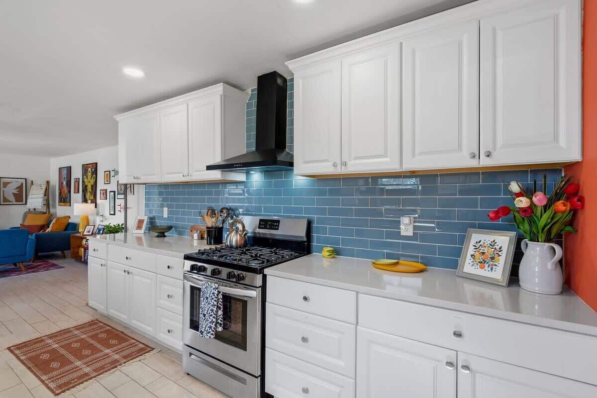Una cocina moderna con armarios blancos, una campana extractora negra y un salpicadero de azulejos azules.