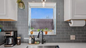 A modern kitchen with grey tiles, a window with plants, a coffee maker, and a sink. - Bright Desert Retreat Pet Friendly (Tucson)