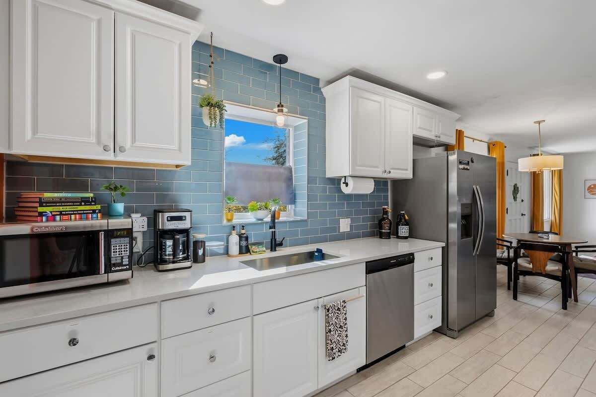 A modern kitchen with white cabinets, a stainless steel refrigerator, a coffee maker, and a window with a view of the sky.