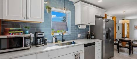 A modern kitchen with white cabinets, a stainless steel refrigerator, a coffee maker, and a window with a view of the sky.