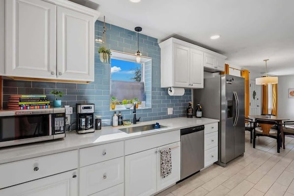 A modern kitchen with white cabinets, a stainless steel refrigerator, a coffee maker, and a window with a view of the sky. - Bright Desert Retreat Pet Friendly (Tucson)