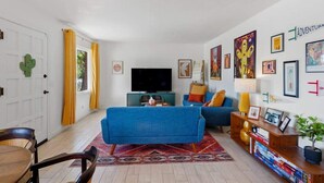 A living room with a blue sofa, a television, and a bookshelf with books. - Bright Desert Retreat Pet Friendly (Tucson)
