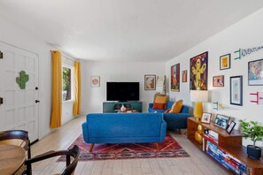 Ein Wohnzimmer mit einem blauen Sofa, einem Fernseher und einem Bücherregal mit Büchern.