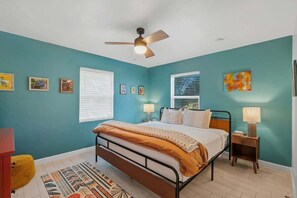 A bedroom with a bed, a ceiling fan, a window with blinds, a bedside table with a lamp, and a rug. - Bright Desert Retreat Pet Friendly (Tucson)