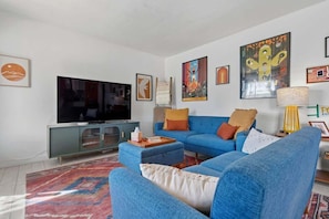 A living room with a large flat-screen TV, blue sofas, a patterned rug, and various wall art. - Bright Desert Retreat Pet Friendly (Tucson)