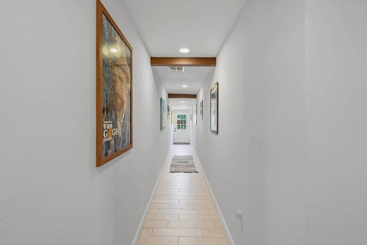 Um corredor com quadros nas paredes, piso de madeira e teto com iluminação embutida.