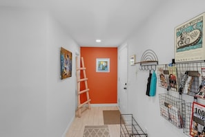 A hallway with an orange accent wall, a wooden ladder, a framed picture, and a rack with various items. - Bright Desert Retreat Pet Friendly (Tucson)