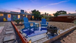 A patio with blue chairs, a fire pit, and a pathway leading to a building. - Bright Desert Retreat Pet Friendly (Tucson)