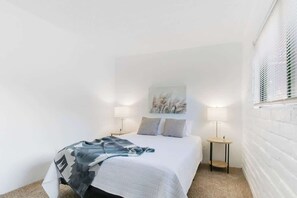 A bedroom with a bed, two bedside tables with lamps, a wall-mounted artwork, and a window with blinds. - Cute Townhome with Community Pool 5 mins to TMC (Tucson)