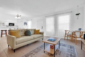 A modern living room with a sofa, coffee table, and dining area. - Cute Townhome with Community Pool 5 mins to TMC (Tucson)
