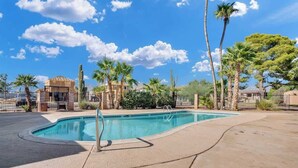 A swimming pool with a curved edge, surrounded by palm trees and cacti, with a clear blue sky above. - Cute Townhome with Community Pool 5 mins to TMC (Tucson)