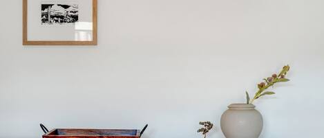 A white cabinet with a framed picture, a wooden tray, and a vase with flowers.