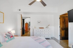 A bedroom with a bed, a dresser, a ceiling fan, and a door leading to another room. - Pet Friendly-Walk to 4th Ave & Downtown! (Tucson)