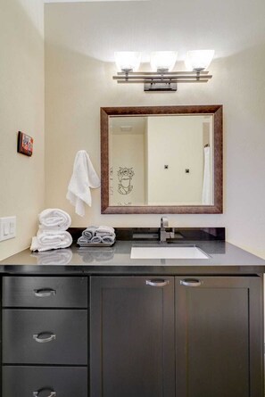 A bathroom with a dark vanity, a mirror with lights, a towel rack, and a sink. - Pet Friendly-Walk to 4th Ave & Downtown! (Tucson)