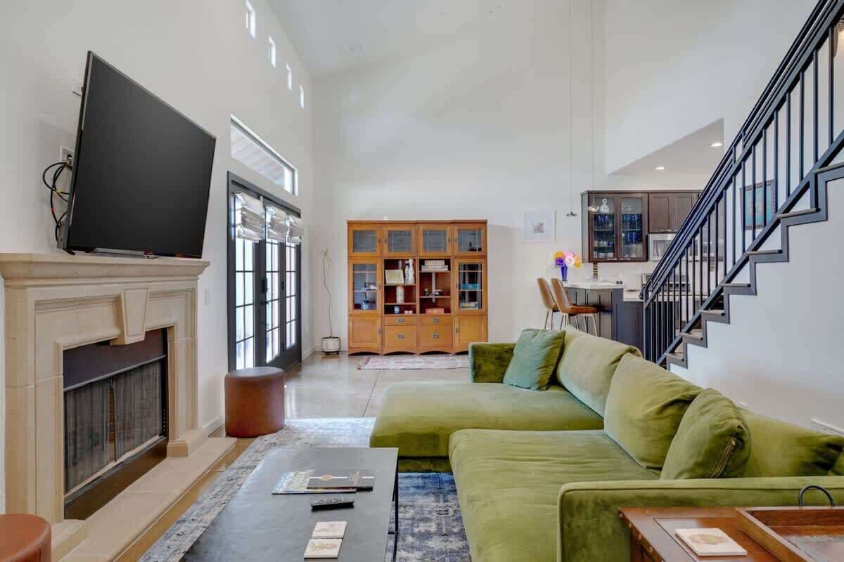 A living room with a green sofa, a fireplace, a television, and a staircase.