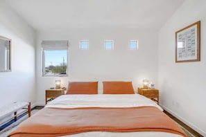 A bedroom with a bed, two bedside tables with lamps, a window, and a framed artwork on the wall. - Pet Friendly-Walk to 4th Ave & Downtown! (Tucson)