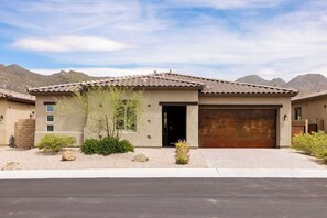 A modern two-story house with a garage, surrounded by a landscaped garden with rocks and shrubs. - Gated Desert Oasis w/ Pool (Marana)