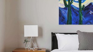 A bedroom with a bed, a nightstand with a lamp, a dresser, and a painting on the wall. - Gated Desert Oasis w/ Pool (Marana)