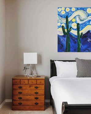 A bedroom with a bed, a nightstand with a lamp, a dresser, and a painting on the wall. - Gated Desert Oasis w/ Pool (Marana)