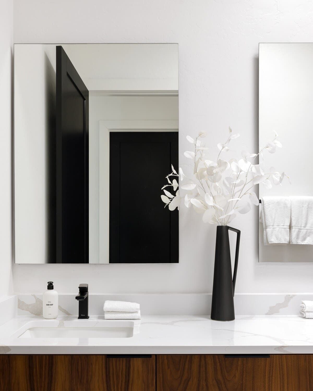 A modern bathroom with a white sink, black faucet, and a vase with white flowers.