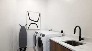 Ett tvättrum med tvättmaskin, torktumlare och ett handfat med en svart kran.