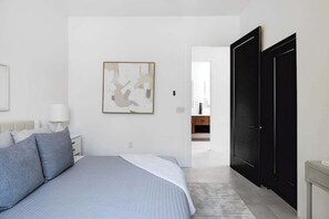 A bedroom with a bed, a nightstand, a lamp, a framed abstract artwork, and a black wardrobe. - Foothills Upscale Retreat with Heated Pool (Tucson)