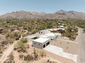 A modern building with a flat roof, a swimming pool, and a desert landscape with mountains in the background. - Foothills Upscale Retreat with Heated Pool (Tucson)