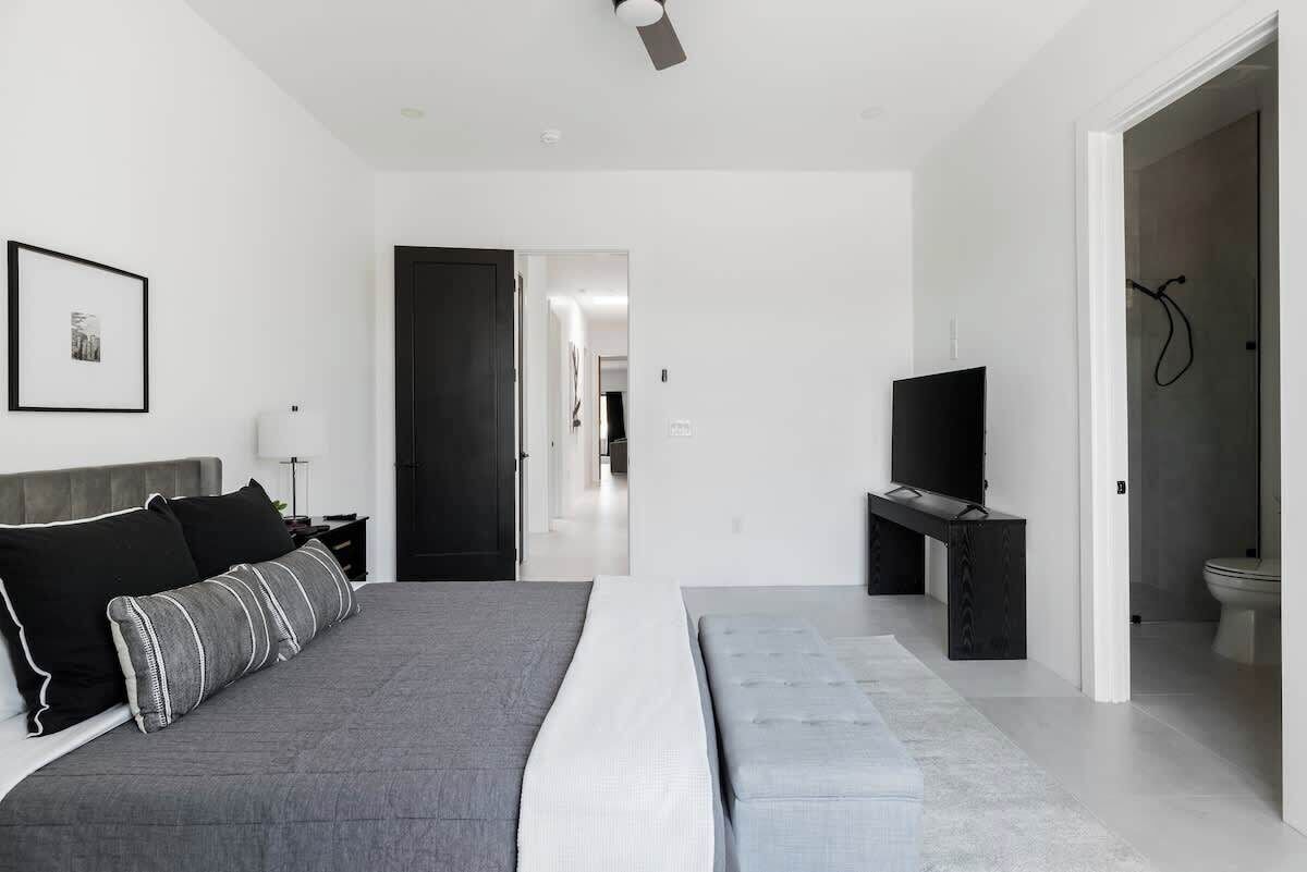 A modern bedroom with a bed, bedside table, TV, and a bathroom visible through an open door.