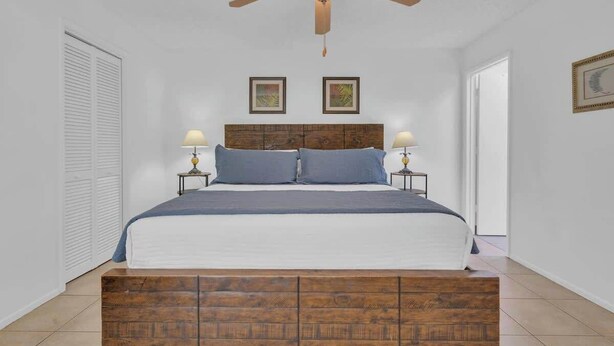 A bedroom with a wooden headboard, two bedside tables with lamps, a ceiling fan, and a white door. - Warm & Quaint Retreat with Pool (Tucson)