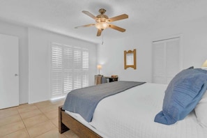 A bedroom with a bed, a ceiling fan, a nightstand, a lamp, and a window with blinds. - Warm & Quaint Retreat with Pool (Tucson)