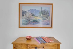 A framed landscape painting, a wooden table with a bowl and magazines, and a wooden cabinet below. - Warm & Quaint Retreat with Pool (Tucson)
